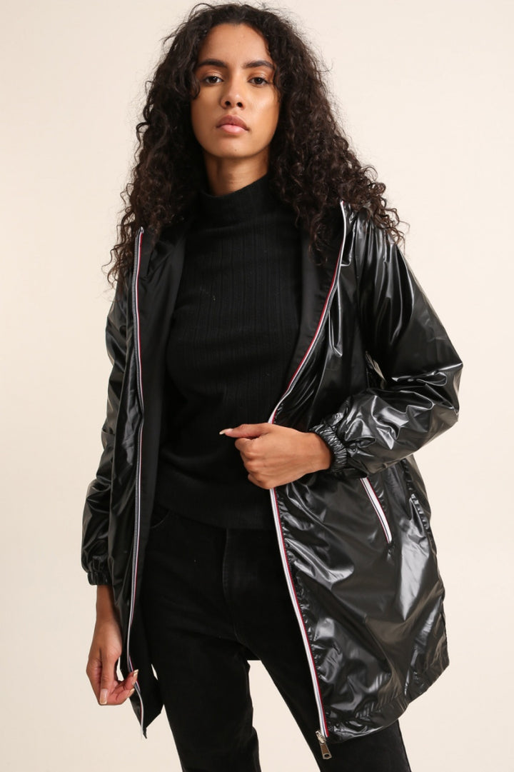 Woman wearing a black shiny raincoat against a beige background